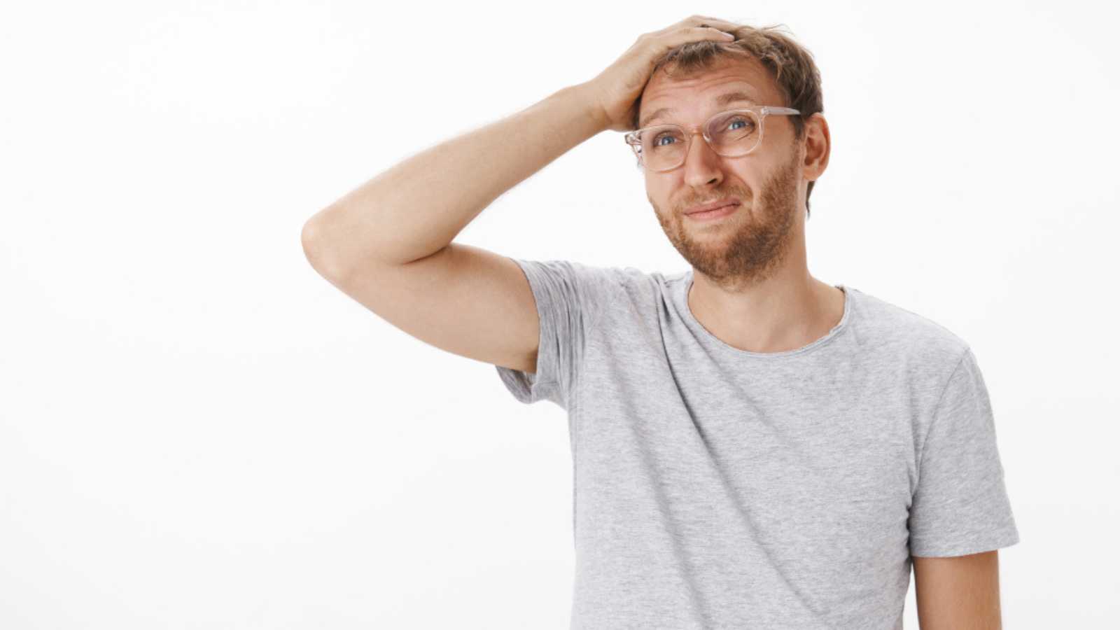 Waist-up shot of silly confused adult father with bristle in glasses scratching top of head smirking and squinting gazing left far away clueless and questioned standing troubled over grey wall