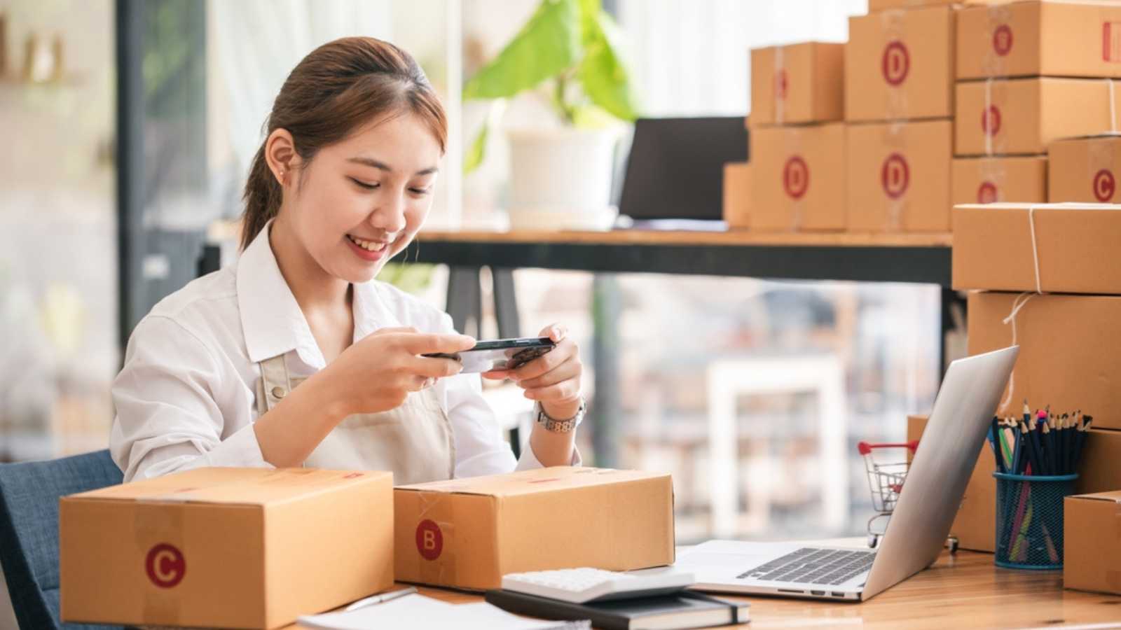 Young woman taking pictures during packaging With a mobile phone or smartphone digital camera to post online sales on the Internet and prepare the product box pack. selling ideas online